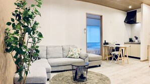 A modern living room with a grey sectional sofa, a round coffee table, and a large potted plant. - Hanazonominami Apartment 101 (Osaka)