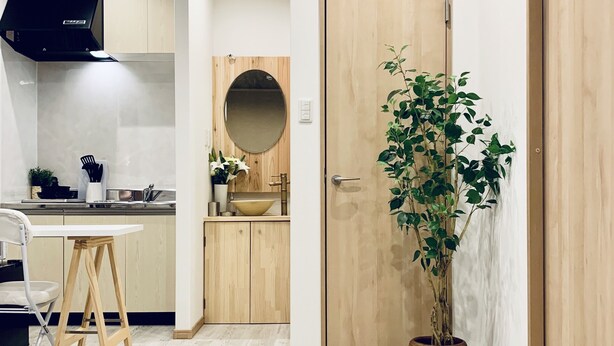 A modern kitchen with wooden cabinets, a round mirror, a sink, and a potted plant. - Hanazonominami Apartment 101 (Osaka)