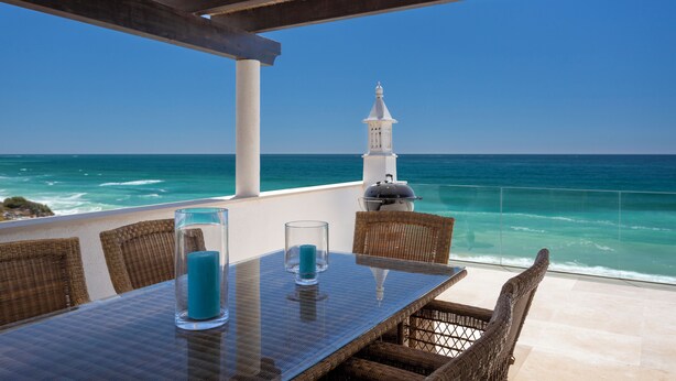 A table with two glasses and a candle, overlooking the ocean with a white tower in the background.