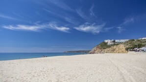 A beach with a clear sky, sandy shore, and buildings on a hillside.
