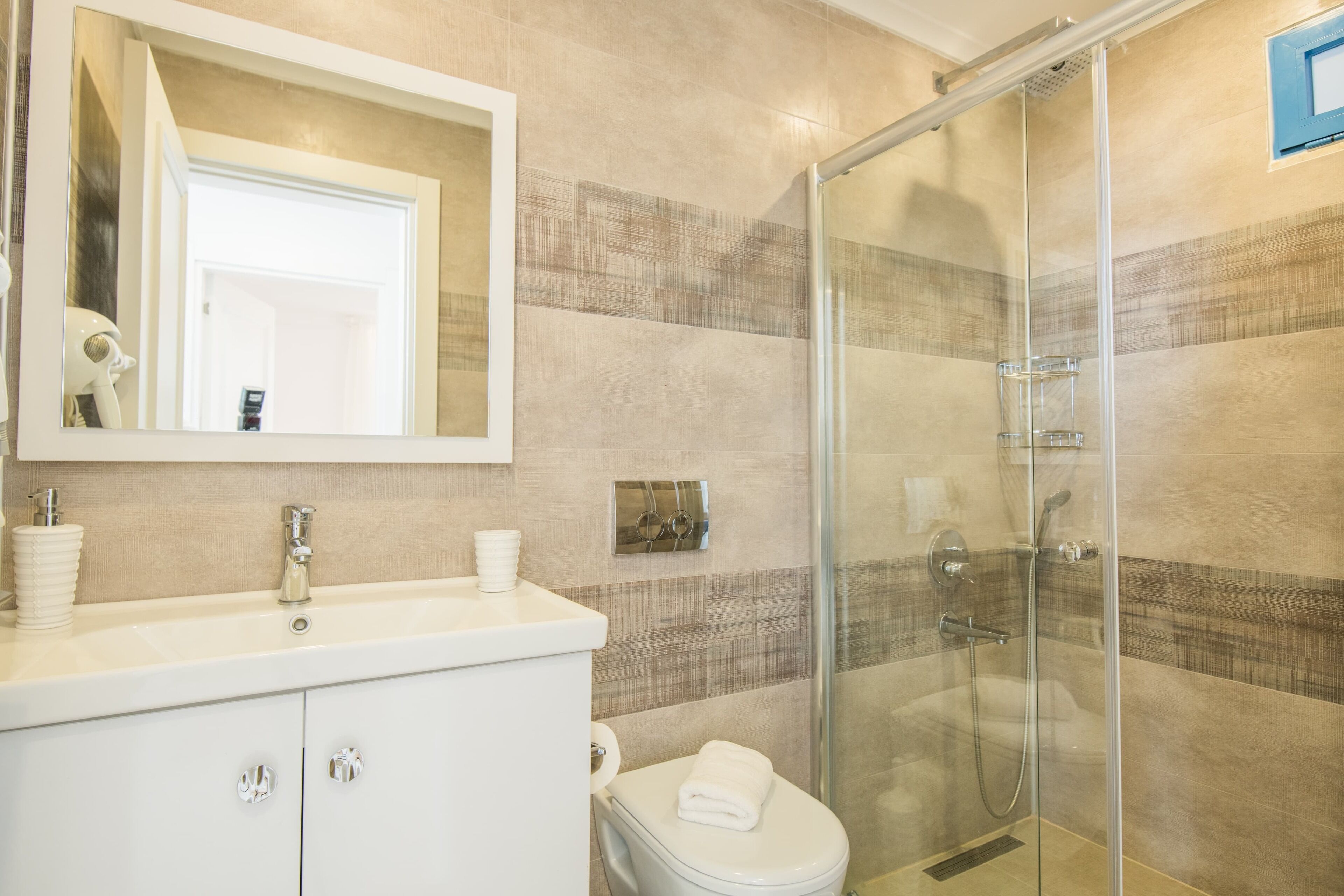 Une salle de bain moderne avec une douche à parois de verre, un lavabo blanc avec un miroir au-dessus et des toilettes.