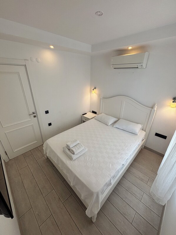 A neatly arranged bedroom with a bed, bedside tables, a door, and an air conditioning unit on the wall.