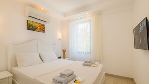 Habitación de hotel con cama, mesita de noche, aire acondicionado, un cuadro, ventana con cortinas y televisor.