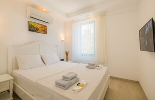 Habitación de hotel con cama, mesita de noche, aire acondicionado, un cuadro, ventana con cortinas y televisor.