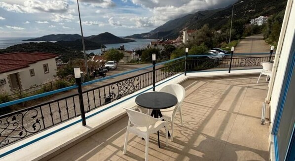 Un balcón con mesa y sillas, con vistas a un paisaje montañoso y una masa de agua.