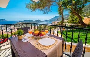 A balcony table set with a fruit bowl, glasses, and a white plate, overlooking a scenic coastal view. -  Carpediem Apart (Kaş)