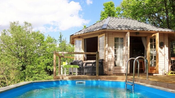 Une cabane en bois avec une piscine, entourée d’arbres.