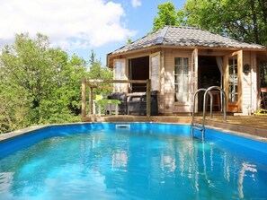 Una cabaña de madera con piscina, rodeada de árboles.