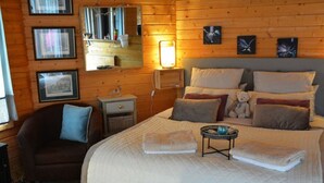 Une pièce confortable avec un grand lit, une chaise, une table de chevet et des tableaux encadrés accrochés au mur.