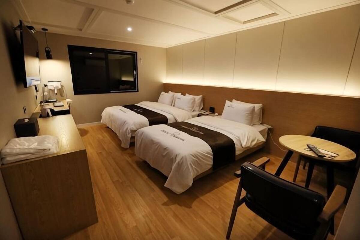 A hotel room with two beds, a desk, a chair, a small table, and a TV.