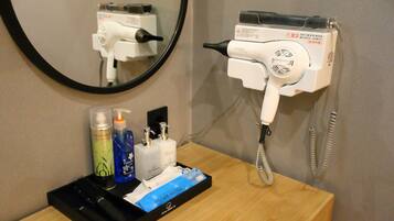 A bathroom with a hairdryer, a mirror, and toiletries on a wooden counter.