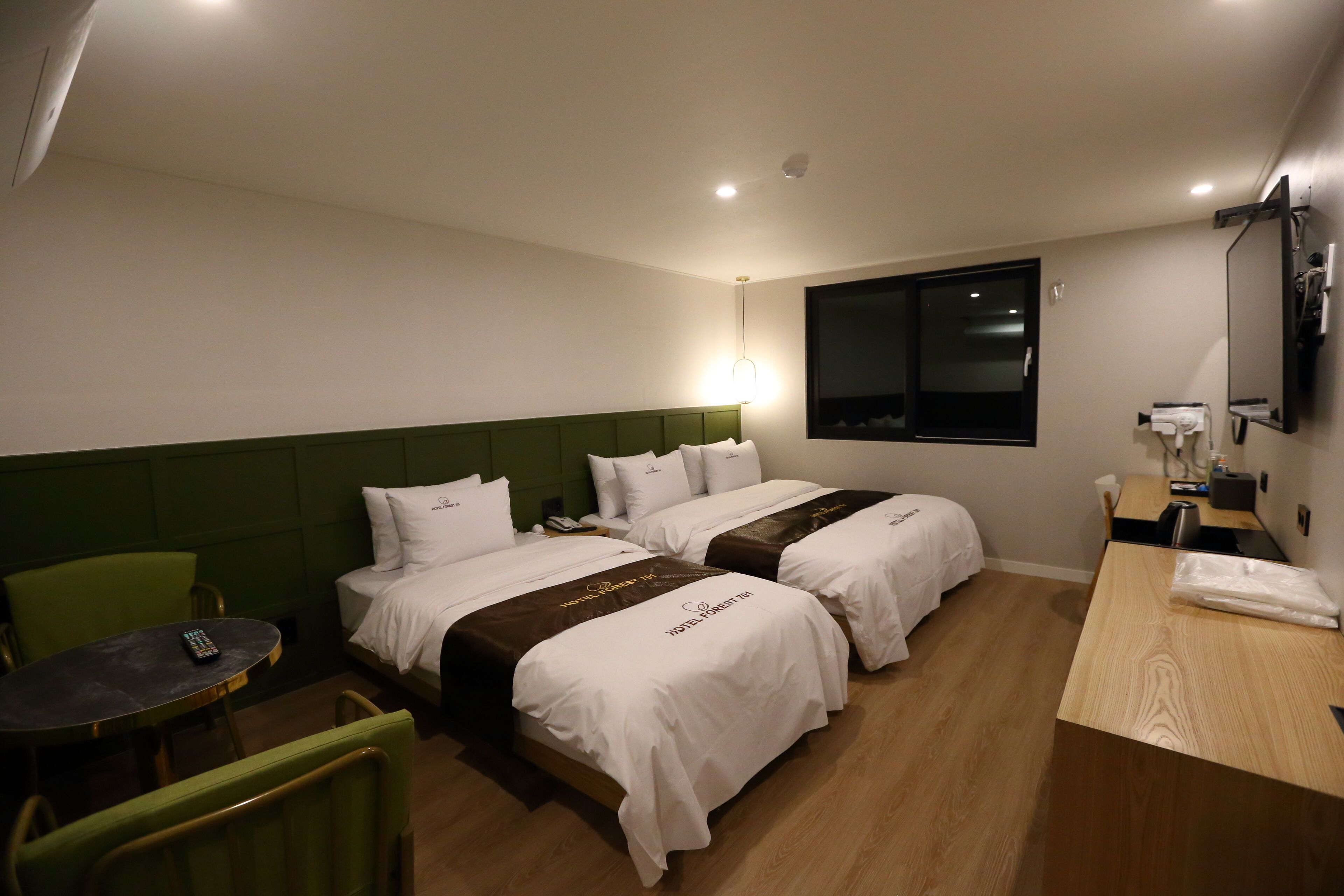 Ein Hotelzimmer mit zwei Betten, einem Schreibtisch, einem Stuhl, einem Tisch und einem Fernseher.