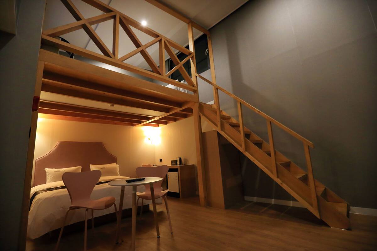 A hotel room with a bed, a desk, a chair, and a staircase.