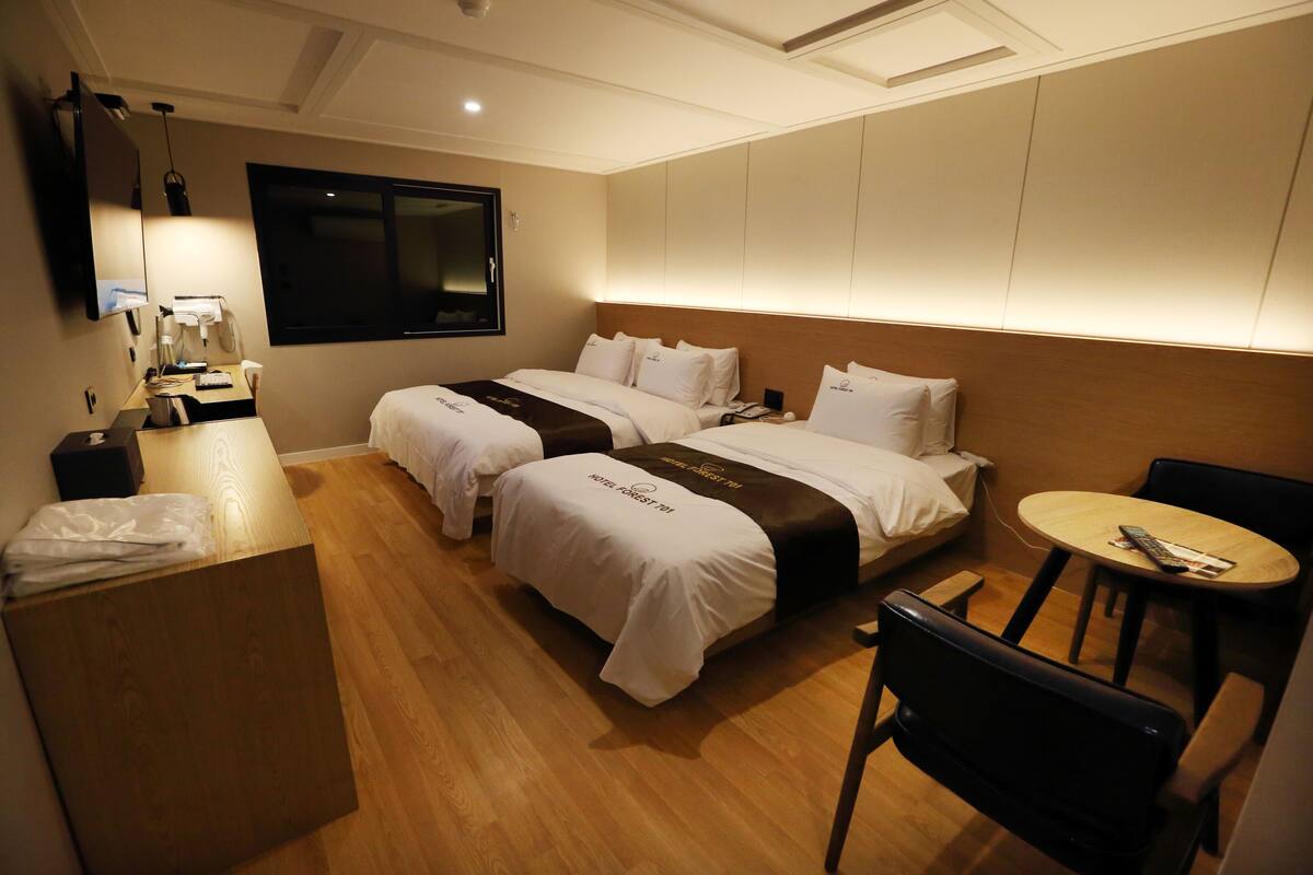 A hotel room with two beds, a desk, a chair, a small table, and a TV.