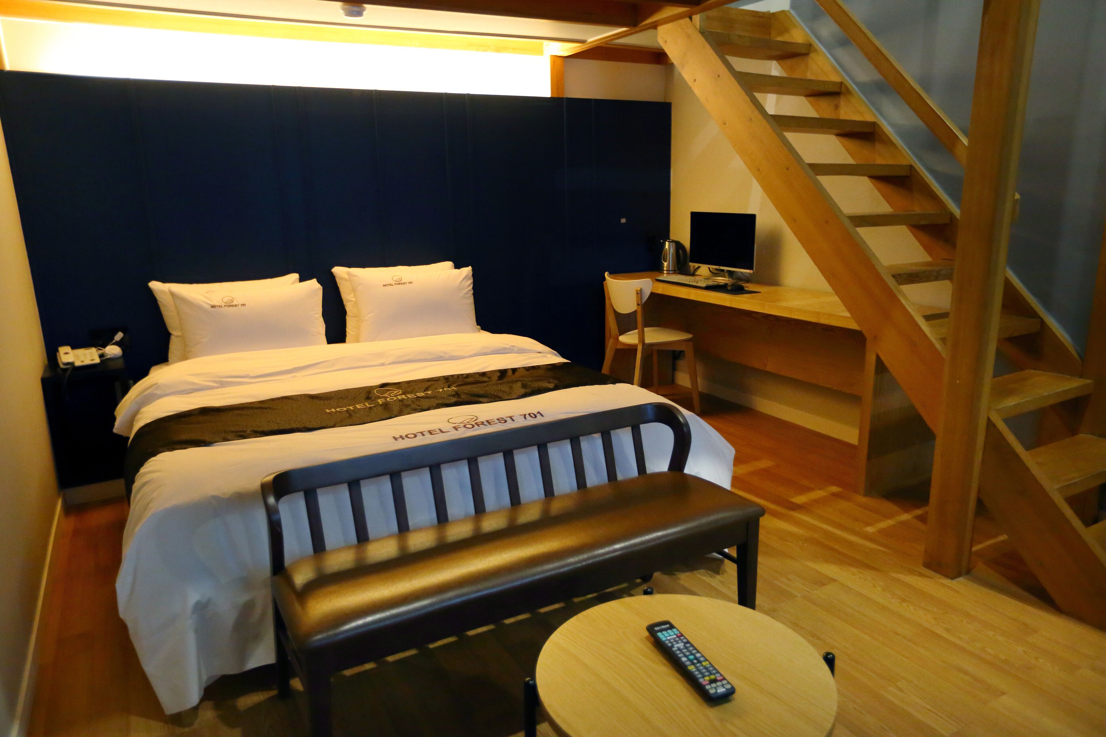 Una habitación de hotel con cama, escritorio, silla, banca, mesa redonda y una escalera.