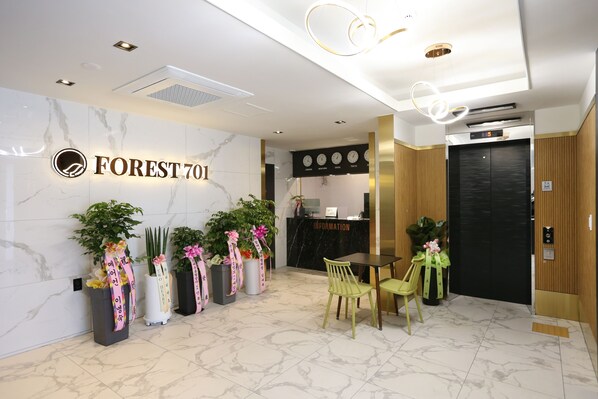 A hotel reception area with a marble wall, a reception desk, a clock, and a wooden elevator.