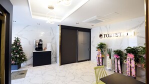 A hotel reception area with a marble floor, a reception desk, a coffee machine, a Christmas tree, and potted plants. - Forest 701 Hotel (Daegu)