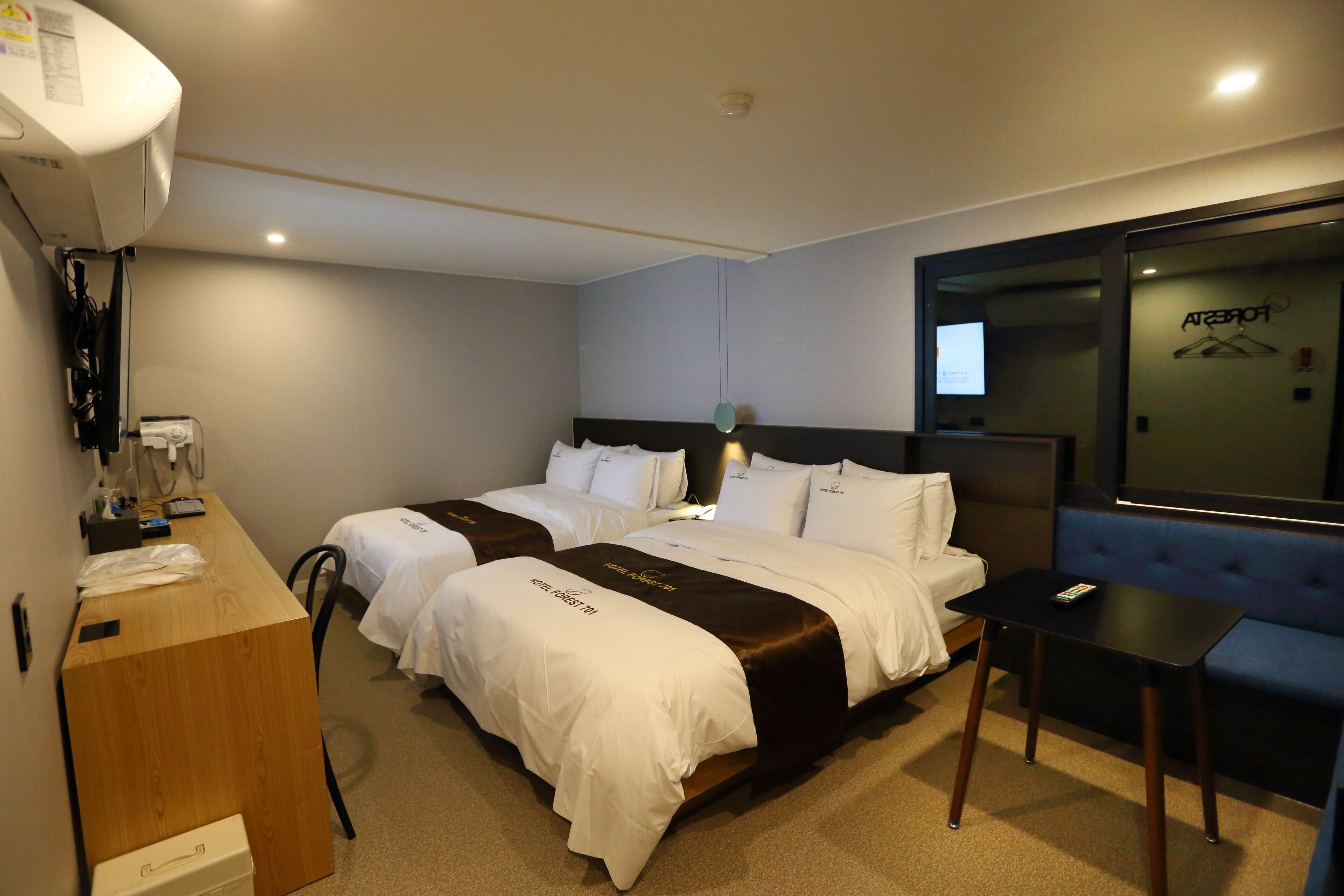 Ein Hotelzimmer mit zwei Betten, einem Schreibtisch, einem Stuhl, einem kleinen Tisch und einem Fernseher.
