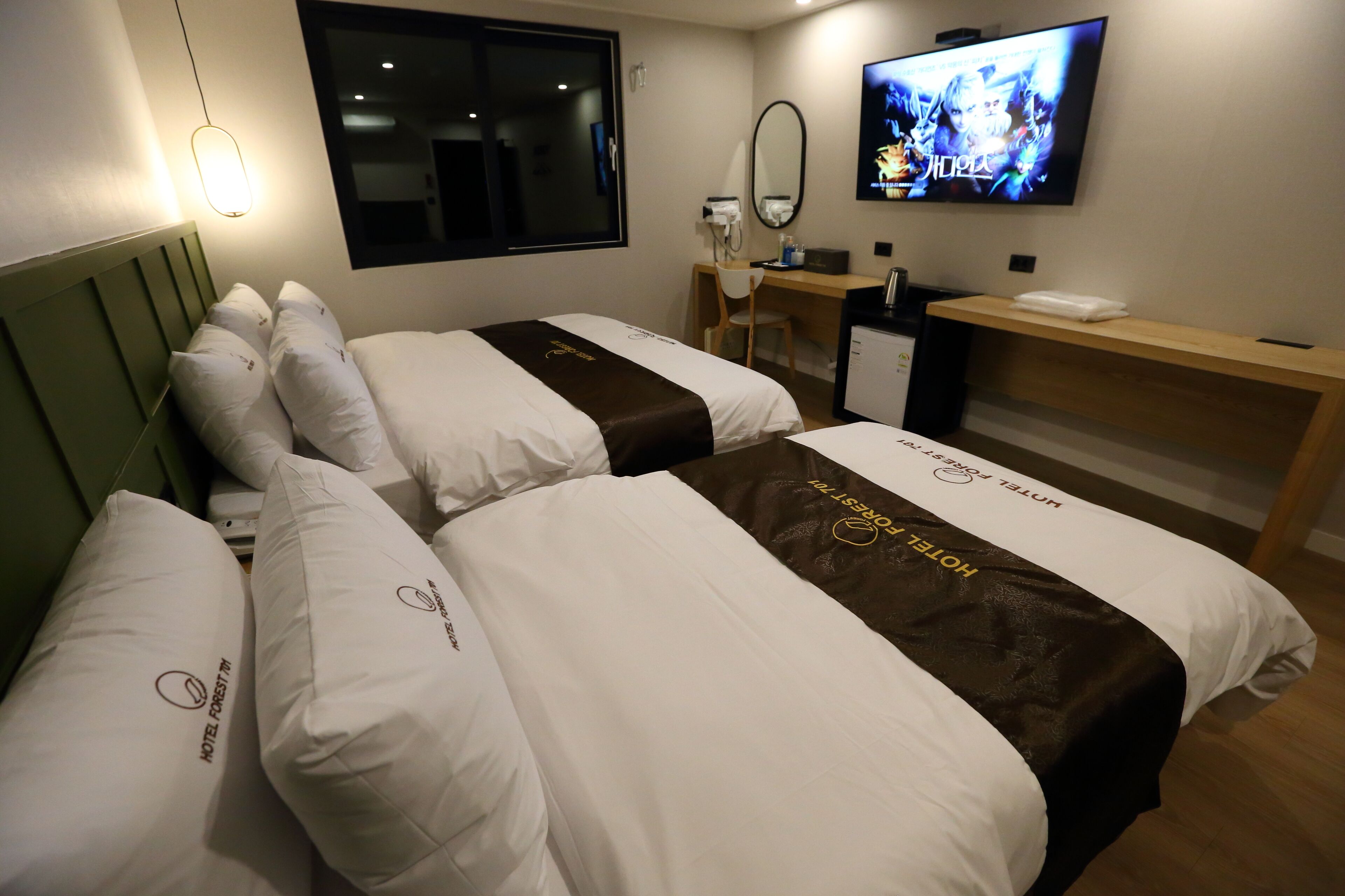 Una camera d'albergo con due letti, una scrivania, una televisione e uno specchio.