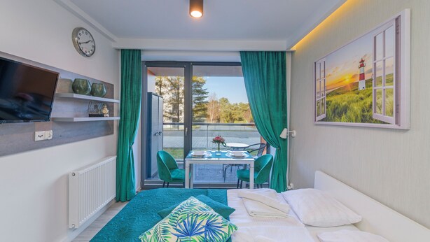A hotel room with a bed, a table with chairs, a TV, and a painting of a lighthouse. - Apartamenty Sun & Snow Sanatoryjna (Wladyslawowo)