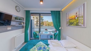 Habitación de hotel con cama, una mesa y sillas, televisión y un cuadro de un faro.
