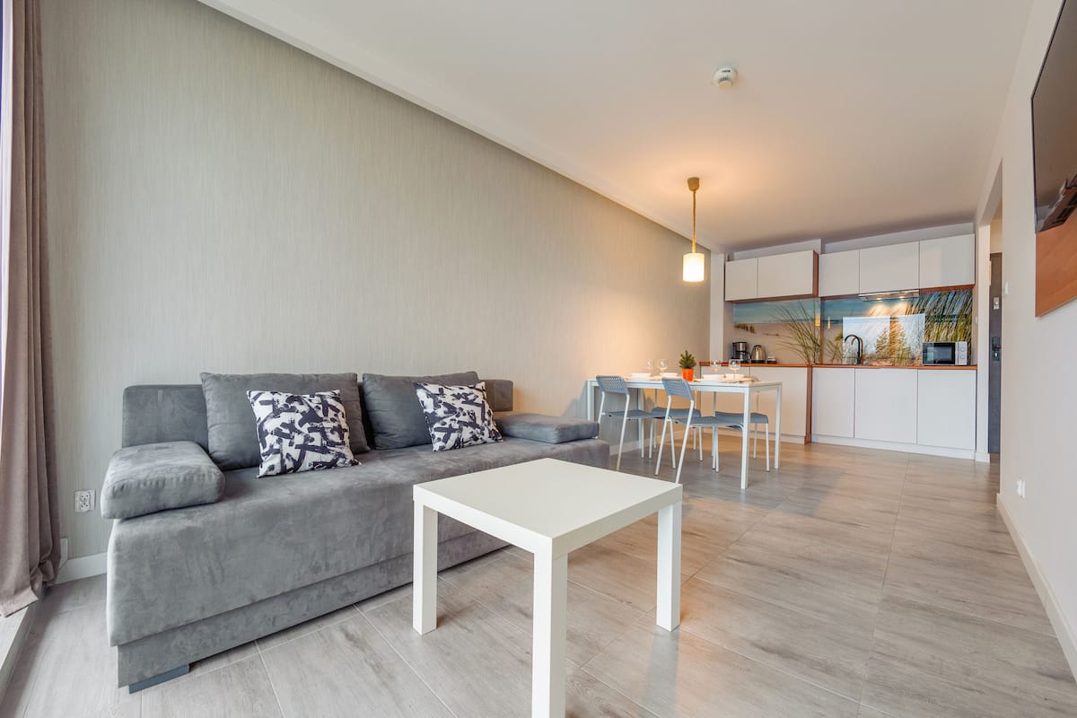 A modern apartment with a grey sofa, white coffee table, and a dining area with chairs and a table.