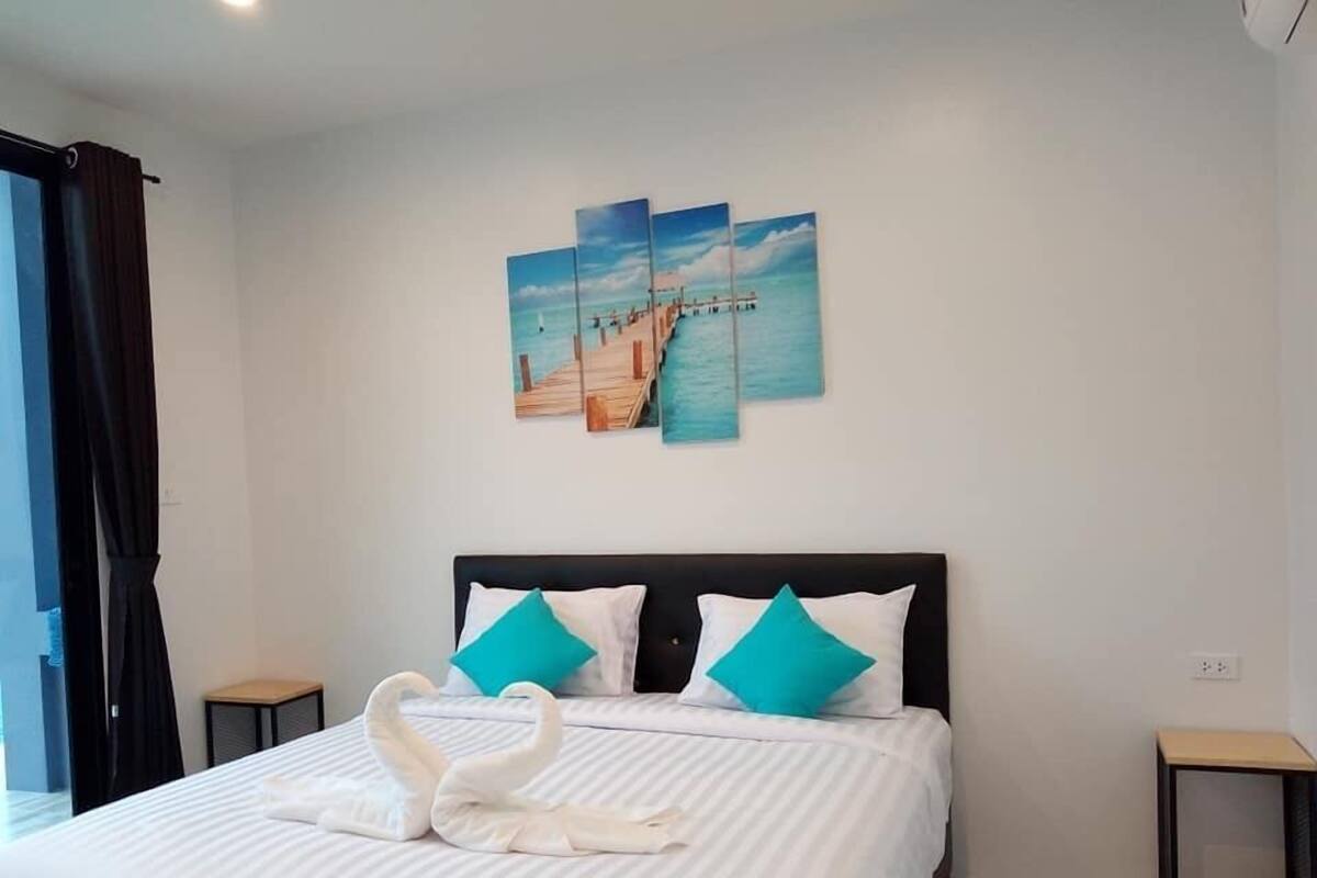 Quarto de hotel com uma cama, um quadro de um cais e uma escultura de toalha em forma de cisne.