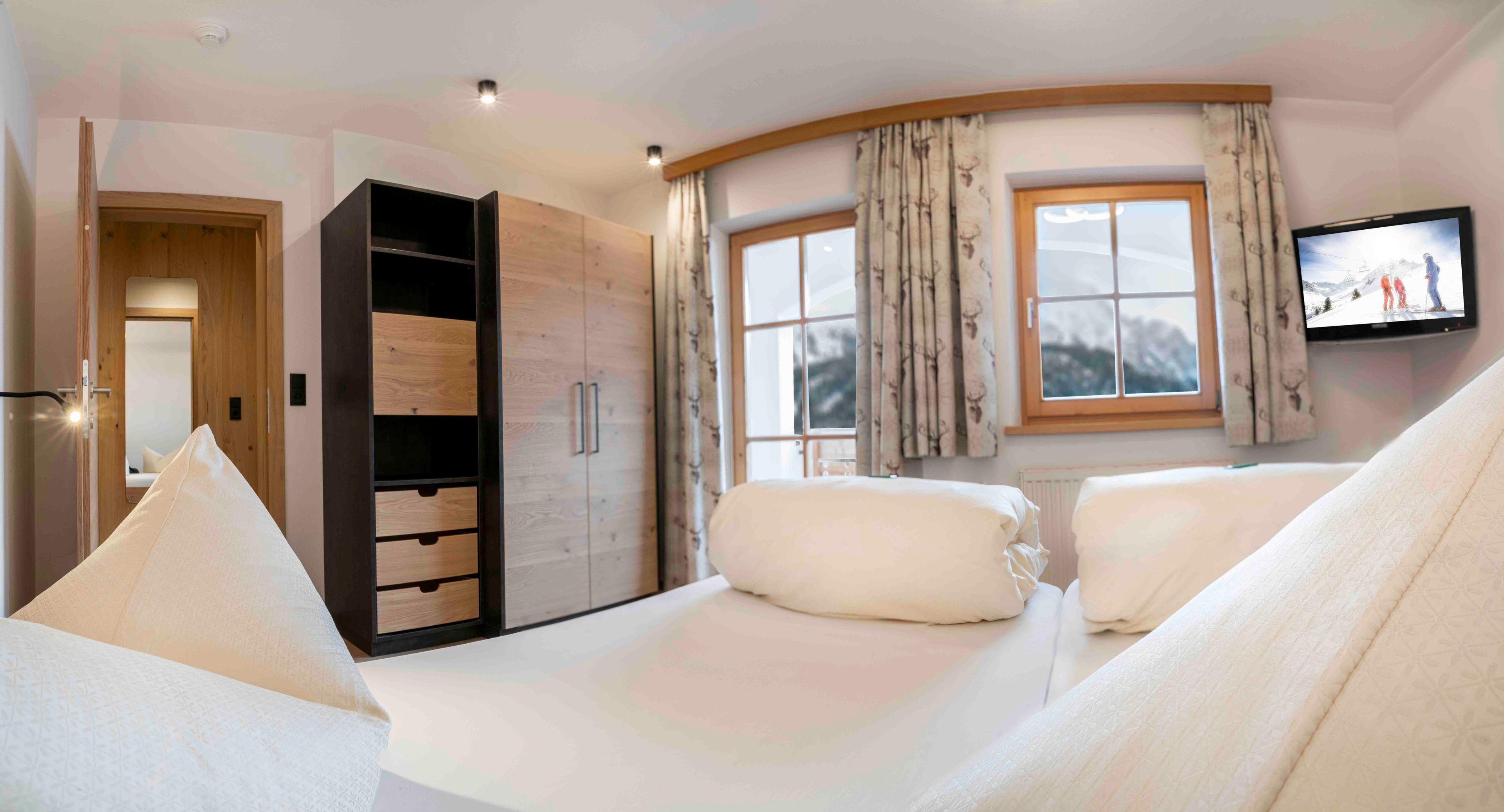 Une chambre d’hôtel avec un lit, une armoire, une télévision et une fenêtre avec des rideaux.