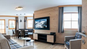 Una sala moderna con un televisor de pantalla plana, un sofá, una silla, una mesa de comedor con sillas y una pared de acento de madera.