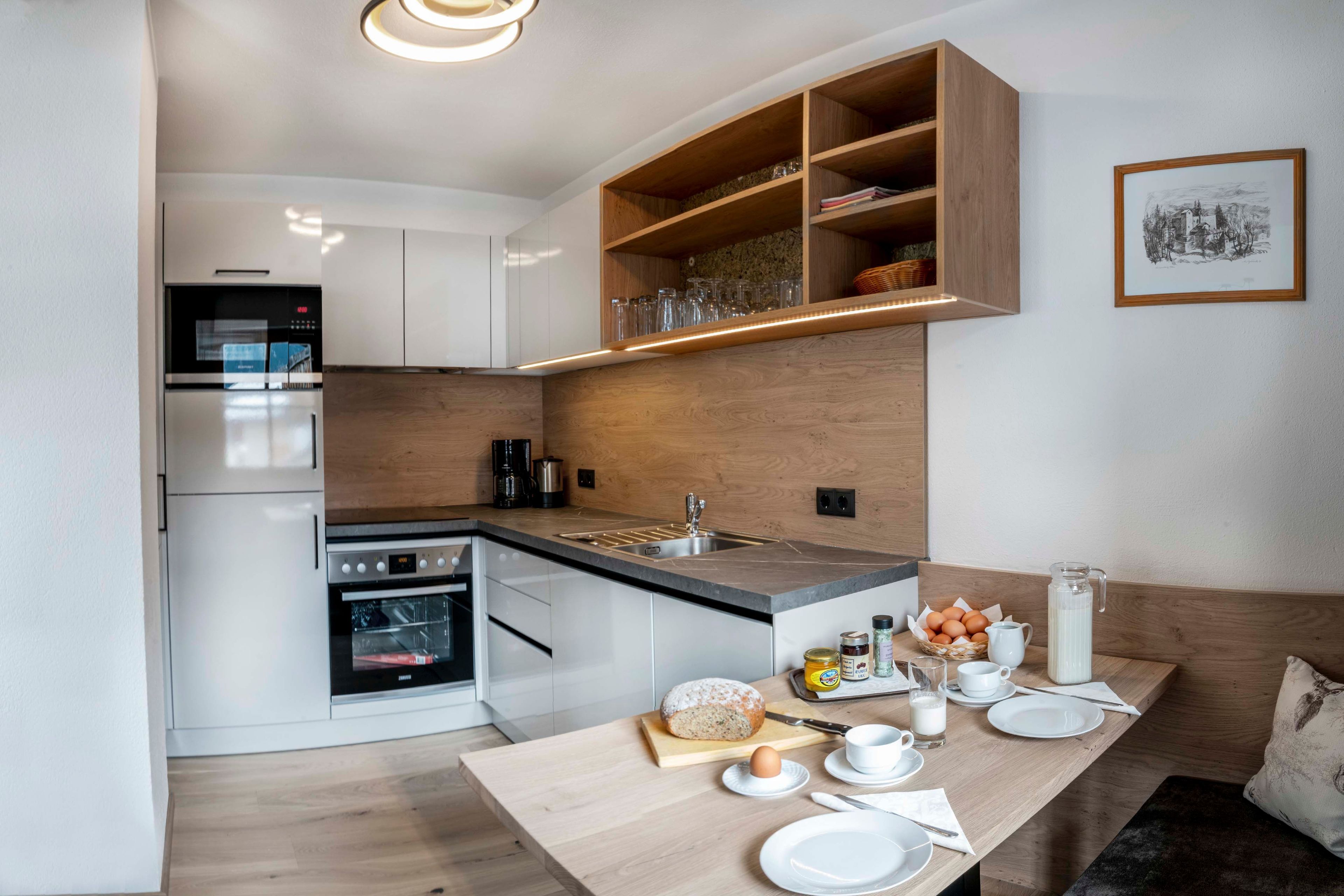 A modern kitchen with built-in appliances, wooden cabinetry, and a breakfast setup on the island.