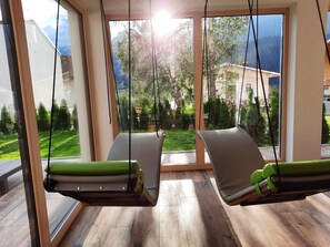 Ein Zimmer mit zwei Hängestühlen, großen Fenstern und Blick auf eine grüne Landschaft.
