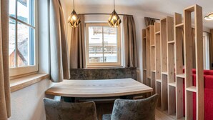 A dining area with a round table, two chairs, a window with curtains, and wooden shelving units. - Vacation apartment Anemone - ROSENHOF Apartments & Wellness & Farmhouse (Nauders)