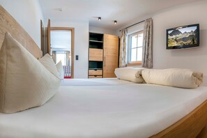 Une chambre à coucher avec un lit, une armoire en bois, une télévision et une fenêtre avec des rideaux.