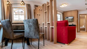 A modern interior with a dining area, a red sofa, wooden shelving, and a television. - Vacation apartment Anemone - ROSENHOF Apartments & Wellness & Farmhouse (Nauders)