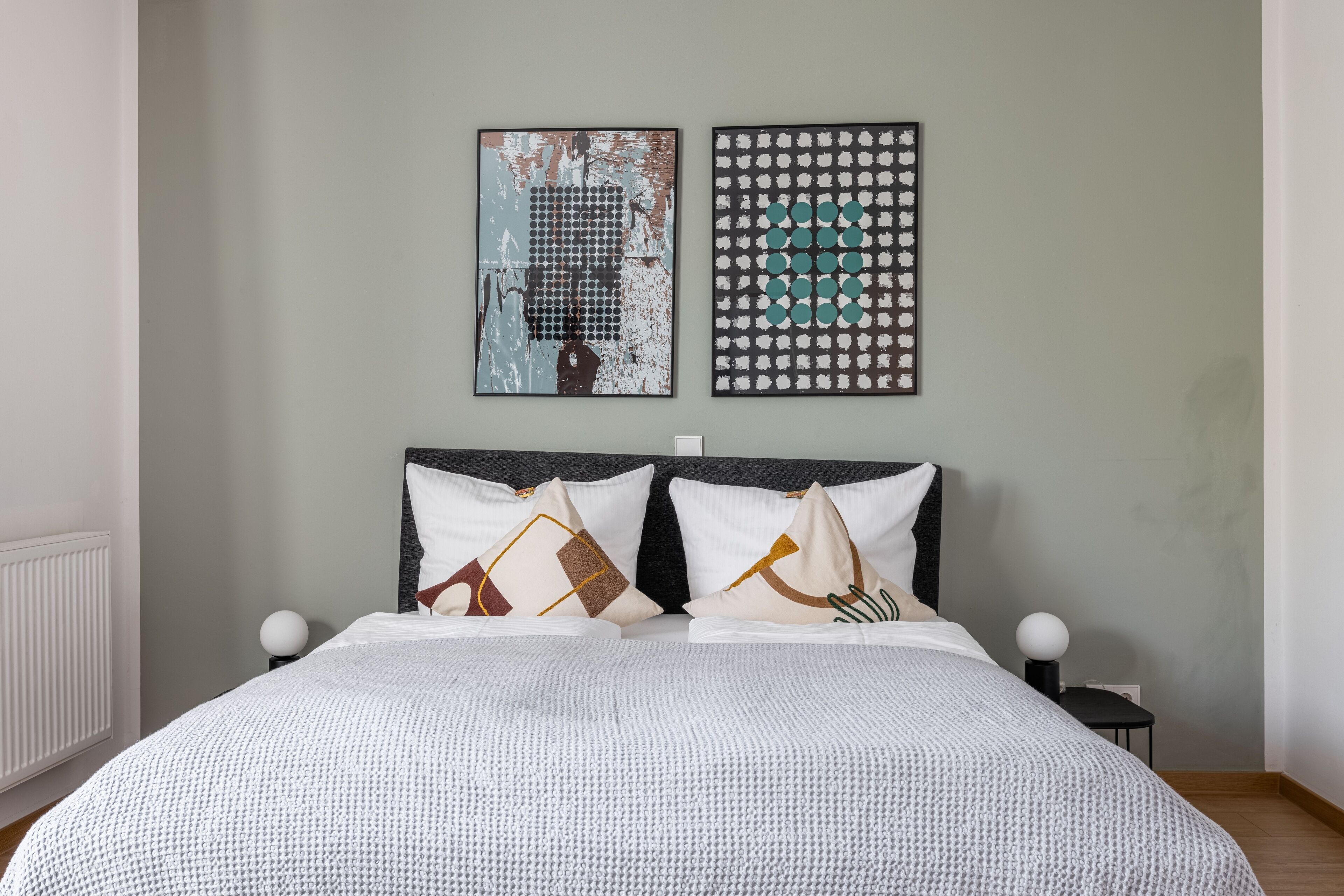 A neatly arranged bedroom with a large bed, two pillows, and two wall-mounted artworks.