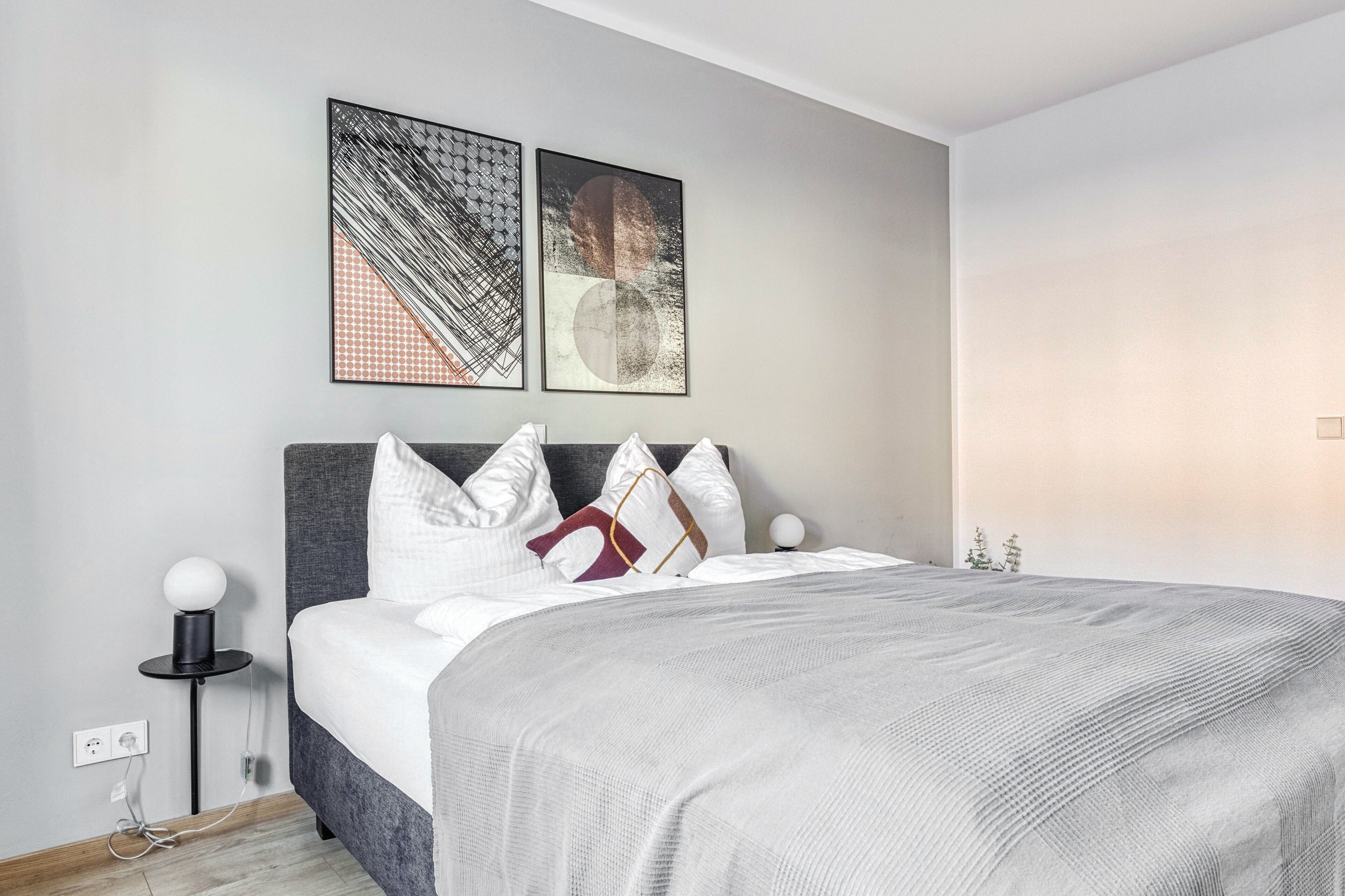 A modern bedroom with a bed, pillows, and artwork on the wall.