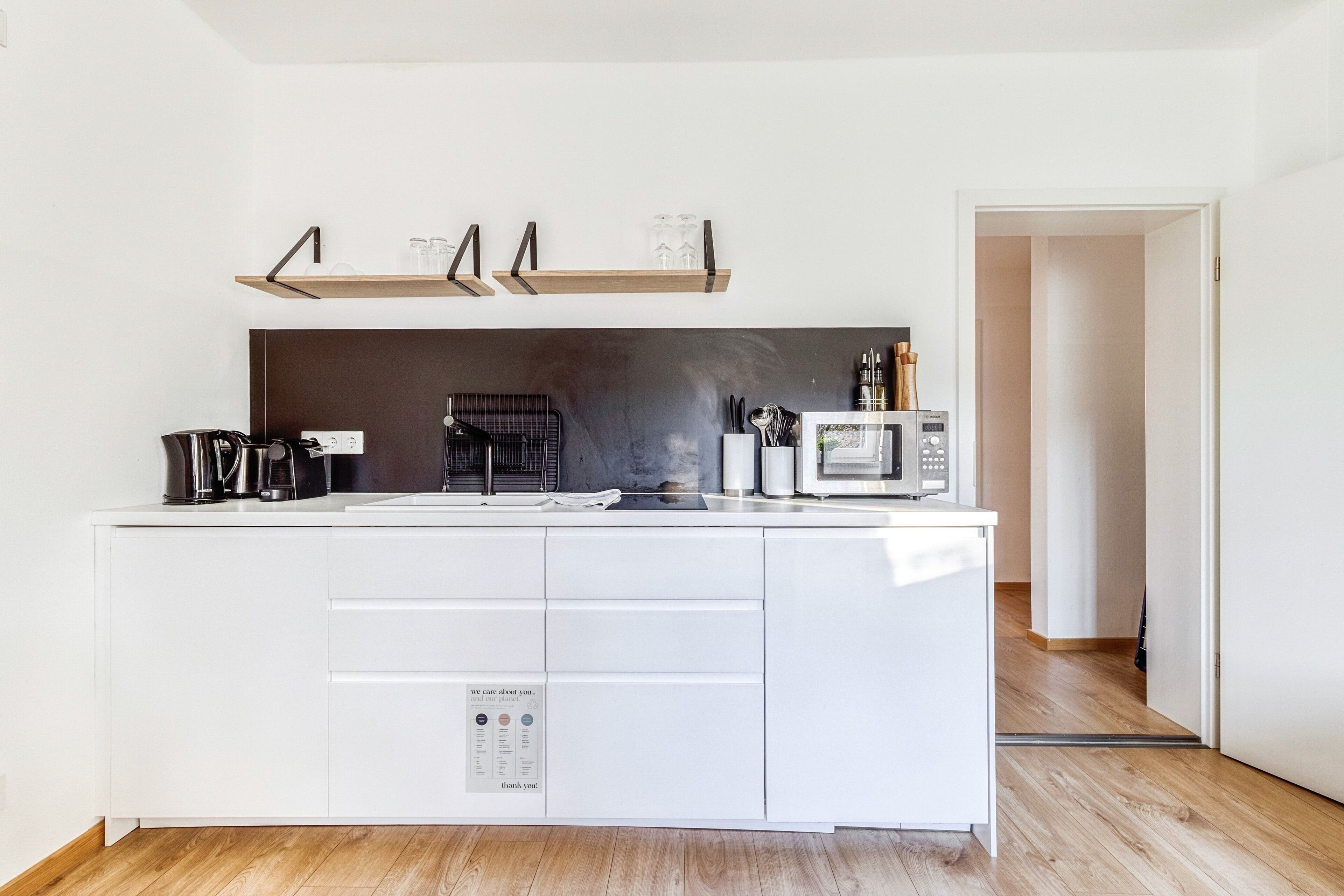 A modern kitchen with white cabinetry, a built-in microwave, and a coffee machine.