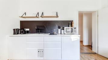 A modern kitchen with white cabinetry, a built-in microwave, and a coffee machine.