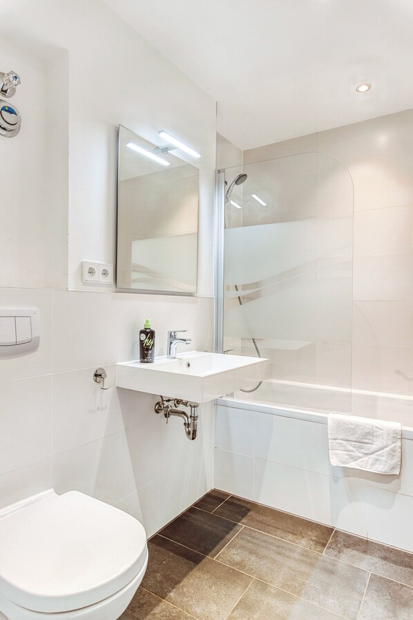 Un baño moderno con inodoro blanco, lavamanos, espejo y ducha con mampara de vidrio.