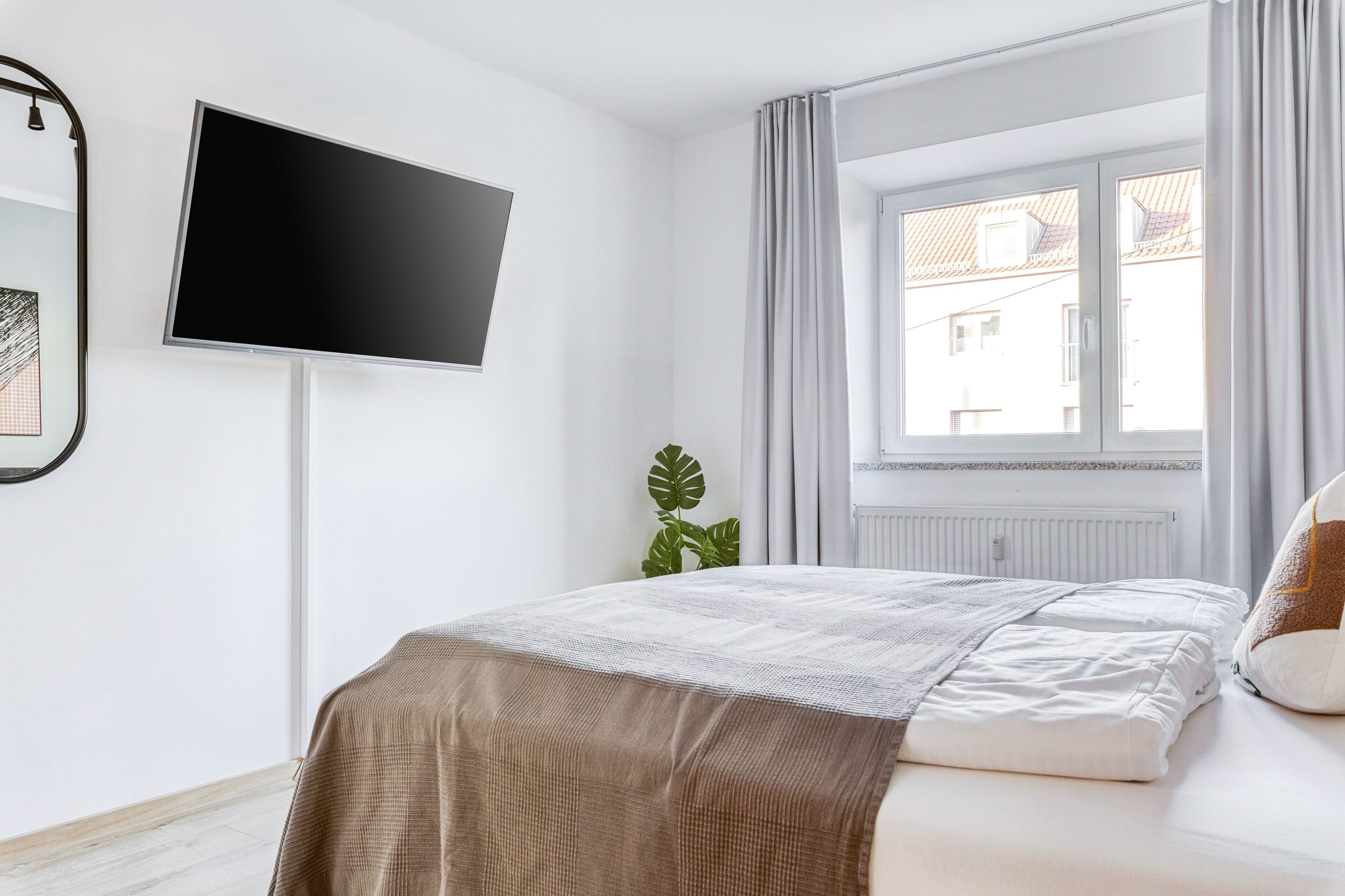 Un dormitorio con cama, televisor montado en la pared, ventana con cortinas y radiador.
