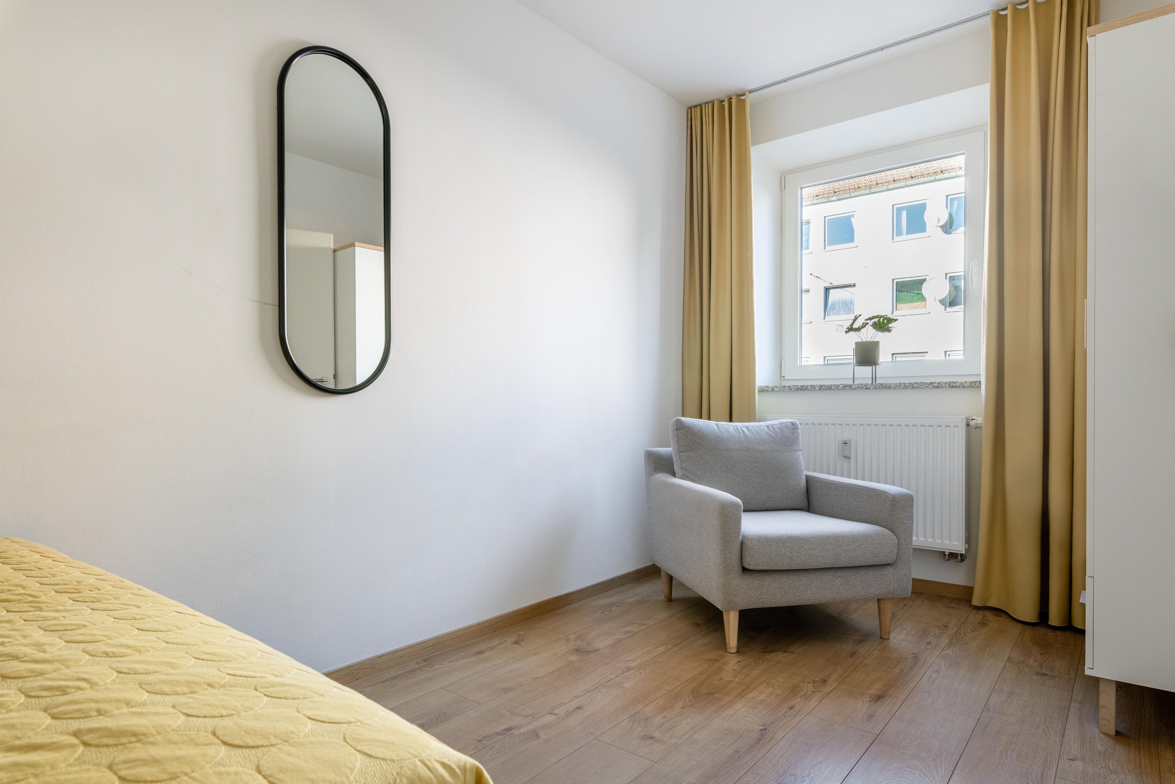 Un dormitorio con cama, una silla, una ventana con cortinas y un radiador.