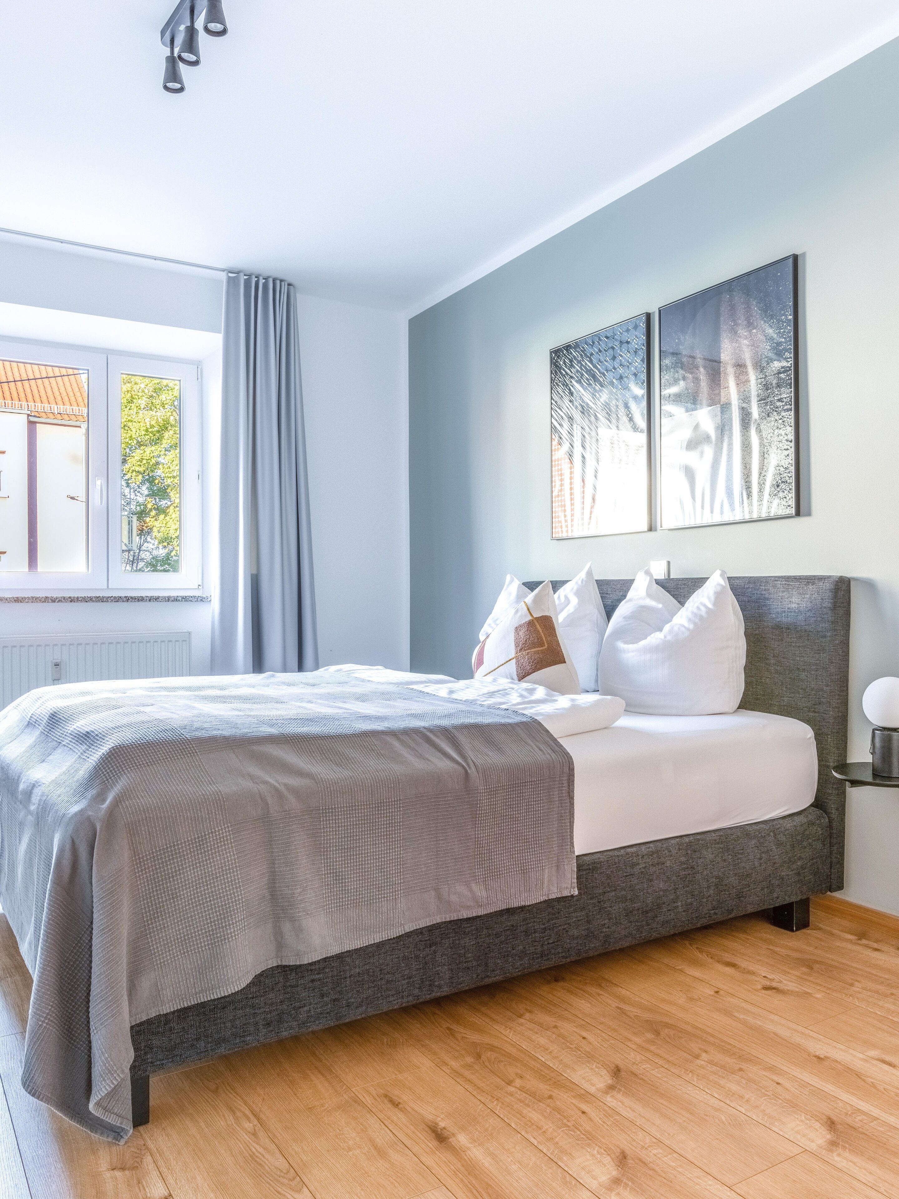 A modern bedroom with a bed, a window with curtains, and a wall with two framed pictures.