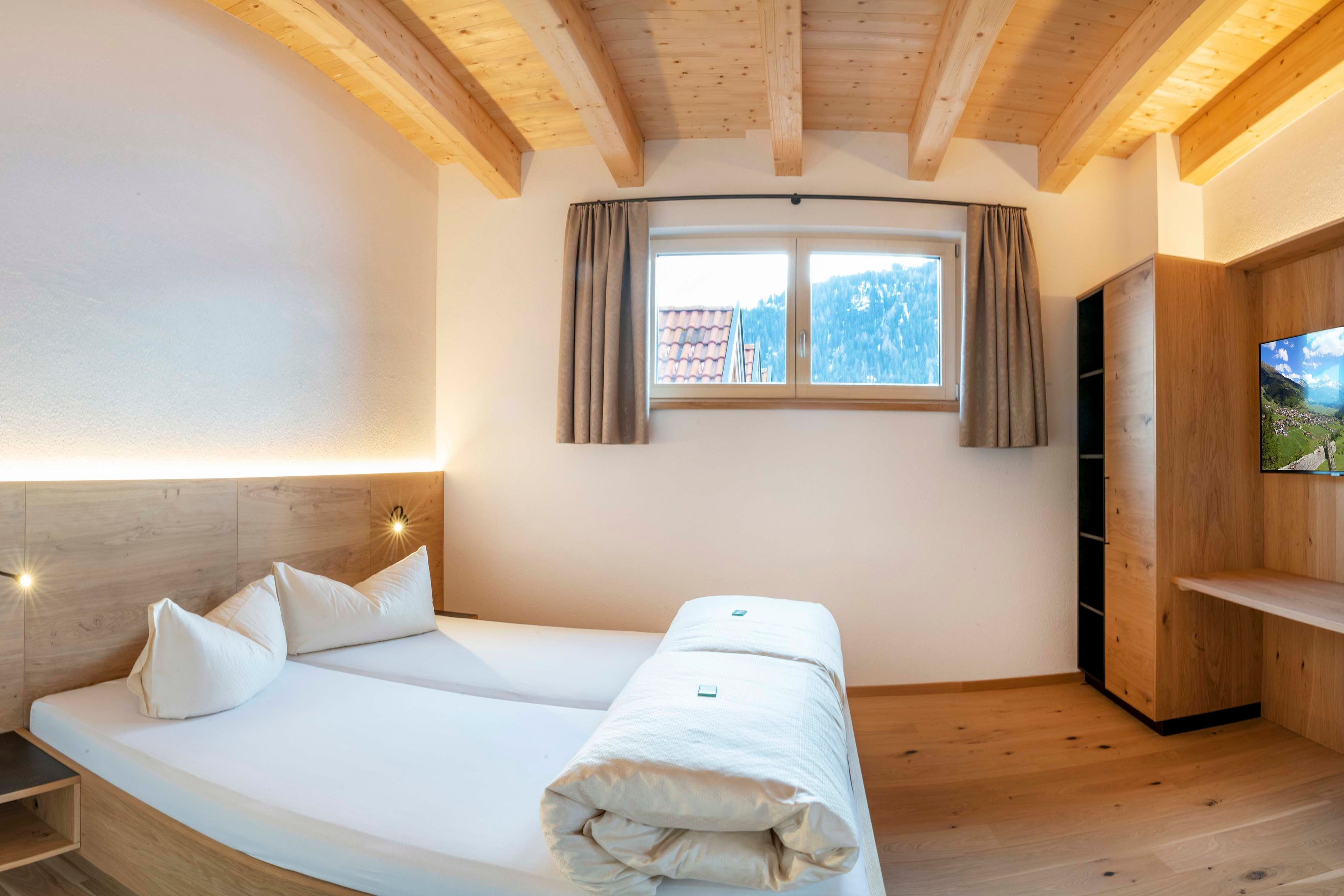 Een slaapkamer met een bed, een televisie, een raam met gordijnen en houten balken in het plafond.