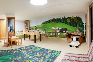 A child's playroom with a mural, a foosball table, a bookshelf, and a stuffed panda. - Vacation apartment Margerite - ROSENHOF Apartments & Wellness & Farm (Nauders)