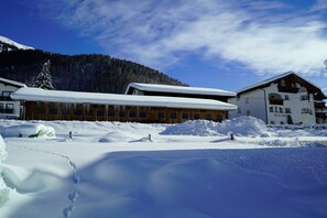 Un edificio cubierto de nieve con fachada de madera, telón de fondo montañoso y cielo despejado.