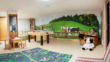 Ein Kinderzimmer mit Wandgemälde, Kicker, Bücherregal und einem Plüschpanda.