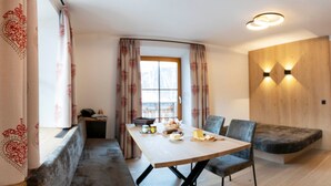 A modern room with a wooden dining table, two chairs, a bench, a small side table with a basket, and a window with curtains. - Vacation apartment Vergissmeinnicht - ROSENHOF Apartments & Wellness & Bauernhof (Nauders)