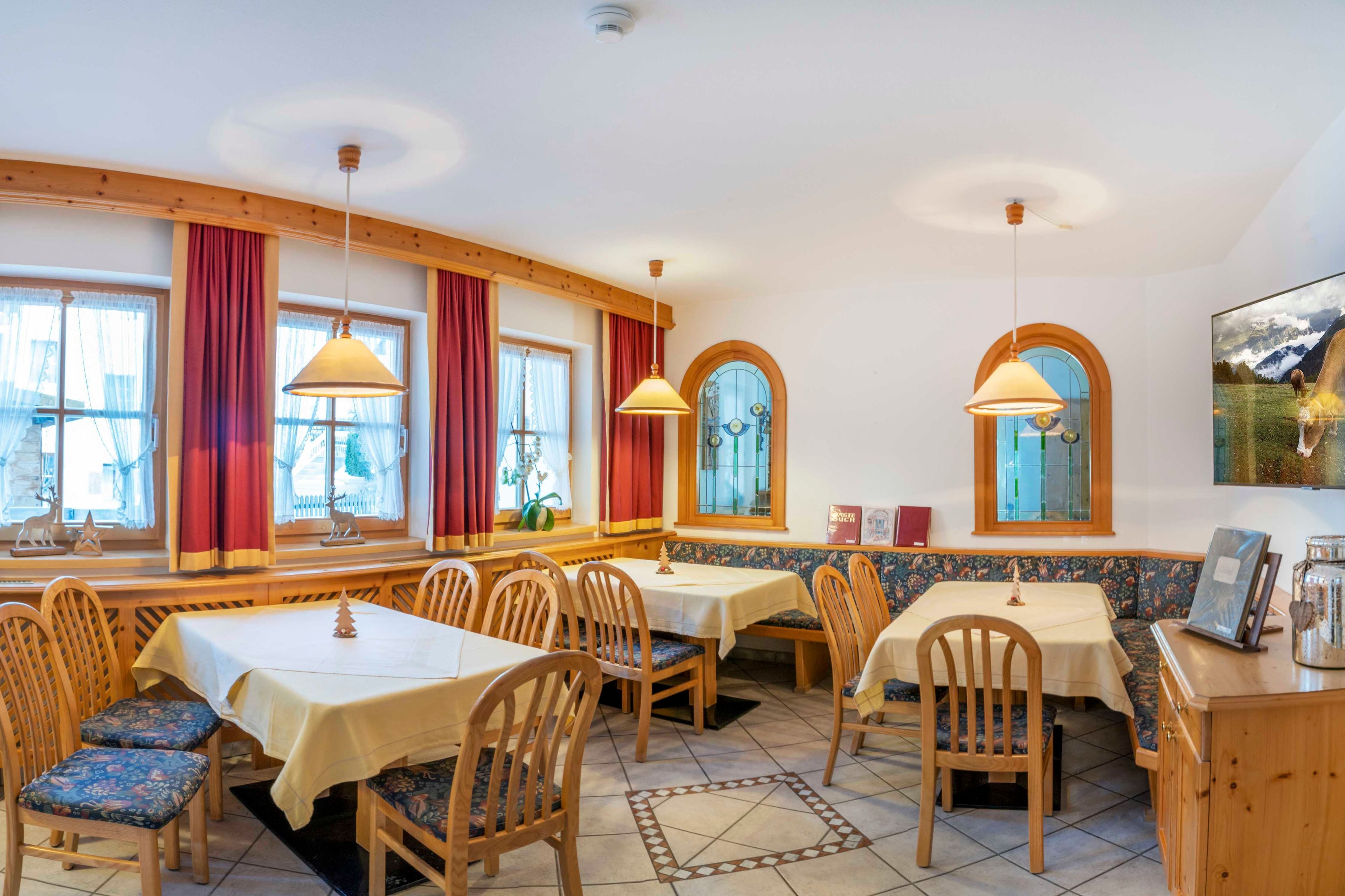 A dining area with wooden tables and chairs, large windows with curtains, and a view of the mountains.
