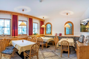 Un comedor con mesas y sillas de madera, ventanas amplias con cortinas y vistas a las montañas.