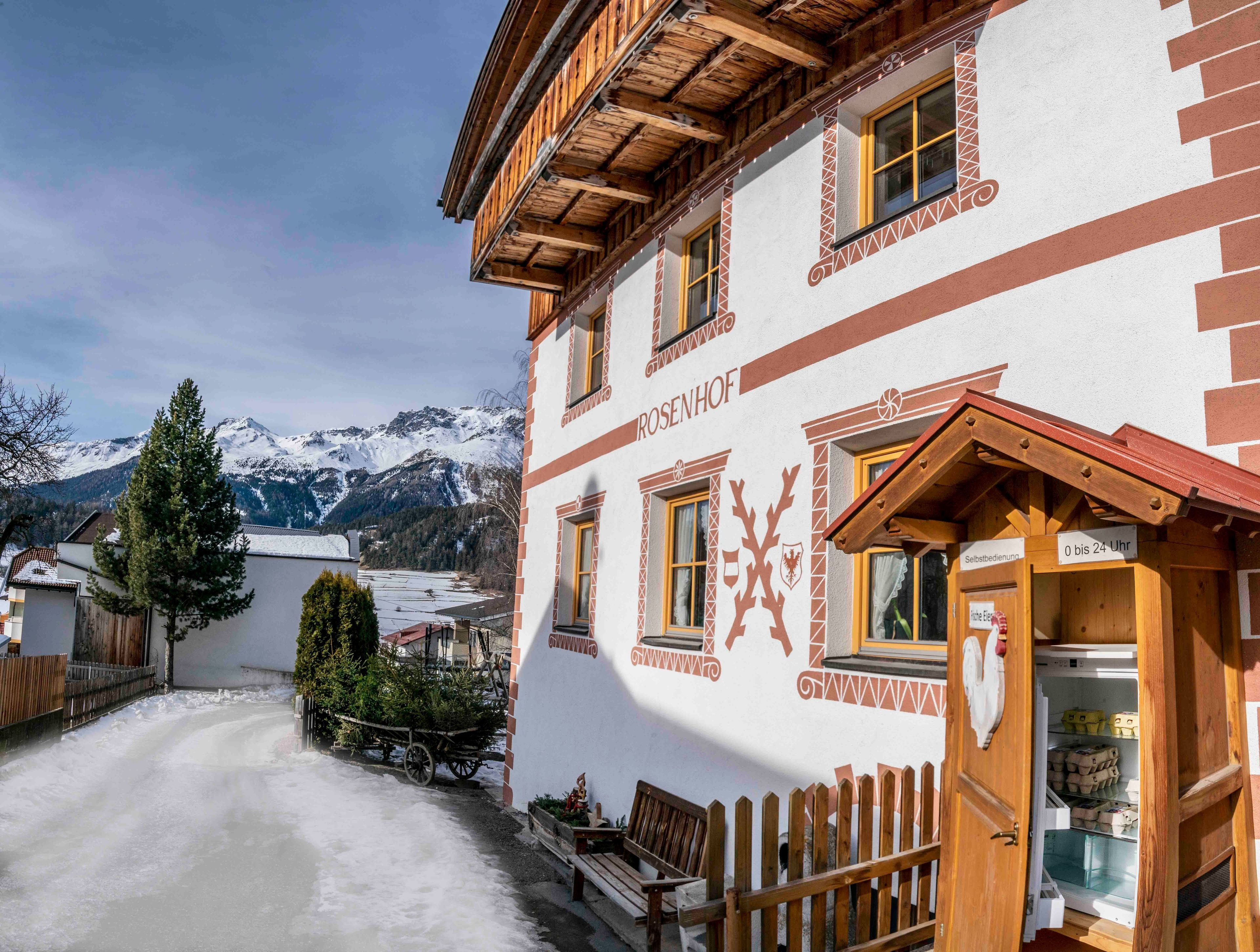 Ein traditionelles Gebäude mit Holzfassade, einem Schild für den 24-Stunden-Service und einem Blick auf schneebedeckte Berge im Hintergrund.